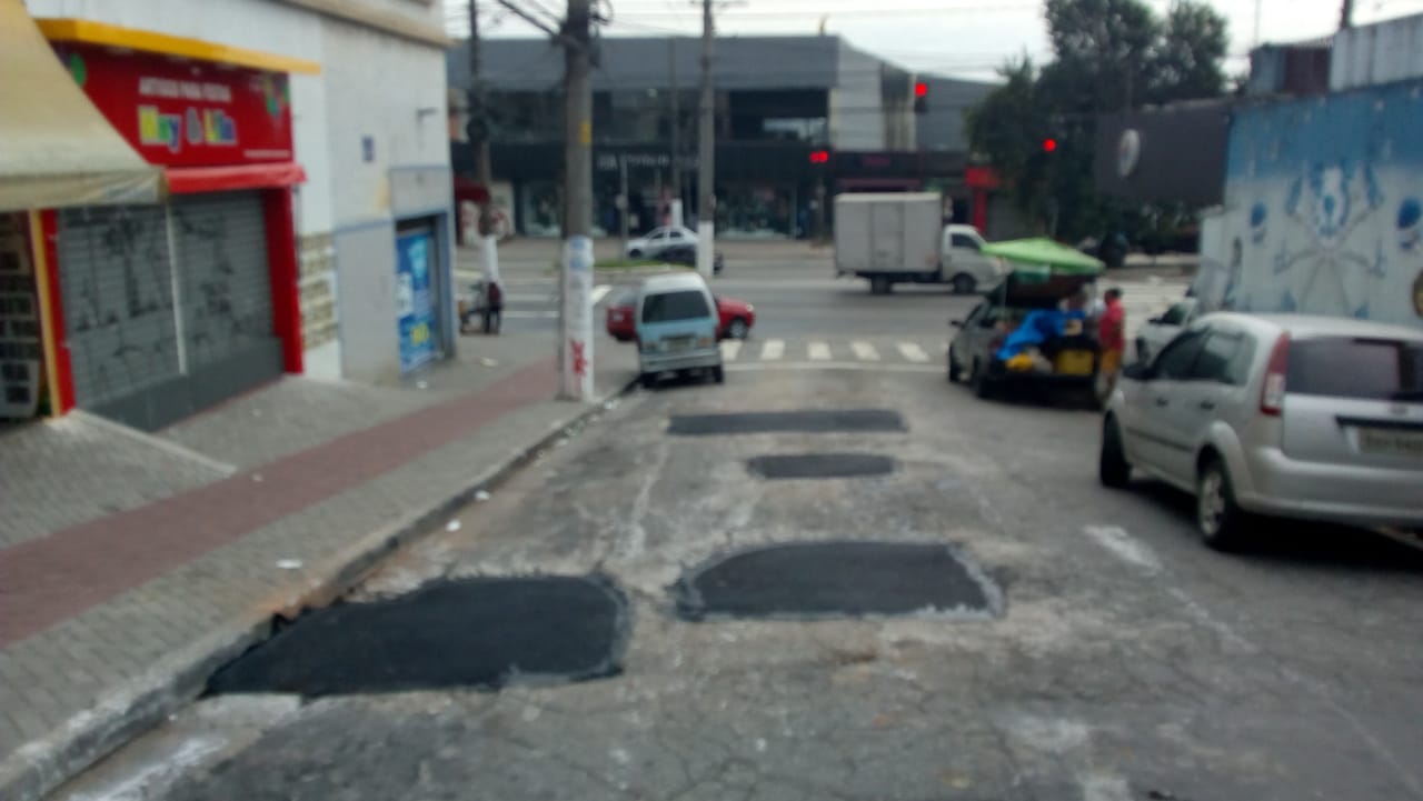 Três marcas de buracos tapados, na rua Abner Ribeiro Borges. O asfalto ficou mais escuro, onde foi feito o remendo. 